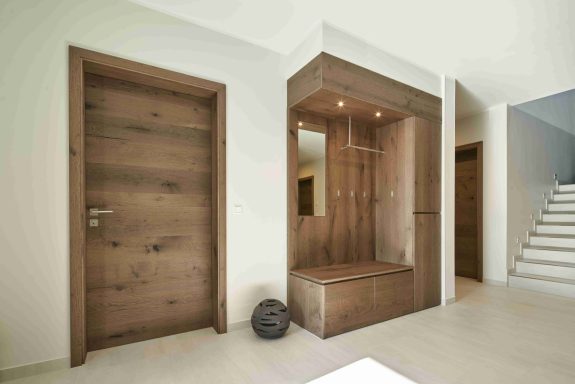 Moderne Eingangshalle mit Holzdetails, Garderobe und Treppe im Hintergrund.