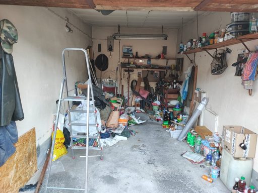 Unordentlicher Garagenraum voller Werkzeuge, Materialien und einem Stehleiter.