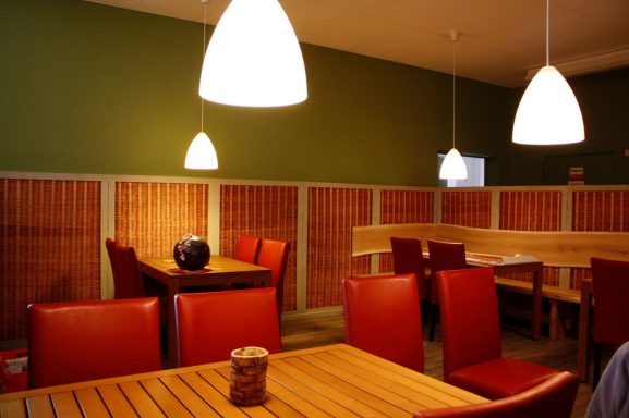 Moderne Restaurantinneneinrichtung mit Holztischen, roten Stühlen und sanfter Beleuchtung.