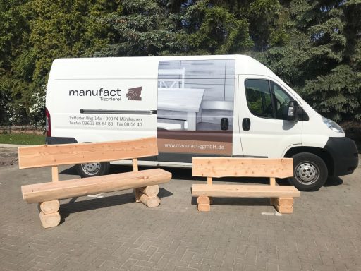 Zwei Holzbänke stehen neben einem weißen Lieferwagen mit Unternehmenswerbung.