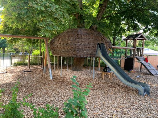 Spielplatz mit Baumhaus, Rutsche und Schaukeln, umgeben von Holzschnitzeln.