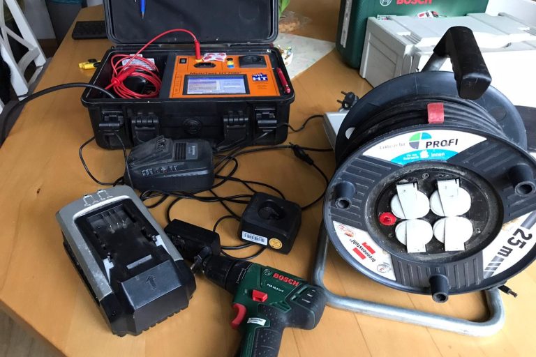 Werkzeuge und Ausrüstung auf einem Tisch: Stromversorgung, Akku, Kabel und Bohrmaschine.