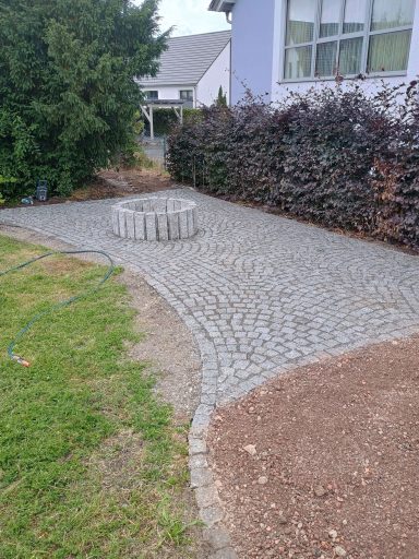 Pflastersteingarten mit einem runden Steinhügel und Büschen im Hintergrund.