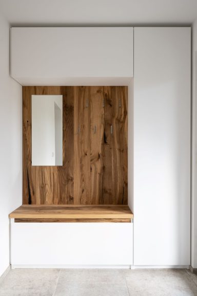 Moderner Flur mit Holzbank und Spiegel, umgeben von weißen Wänden und Möbeln.
