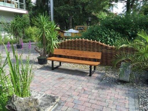 Ruhige Bank aus Holz in einem begrünten Außenbereich mit Pflanzen und Steinen.