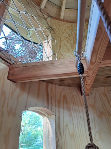 Innenraum einer Baumhütte mit Holzdecke, Seil und Fenster im Hintergrund.