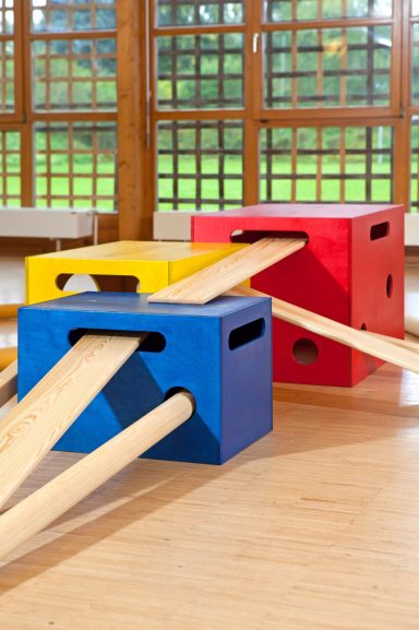 Bunte Kisten in Rot, Gelb und Blau mit Holzplanken in einem Spielraum.