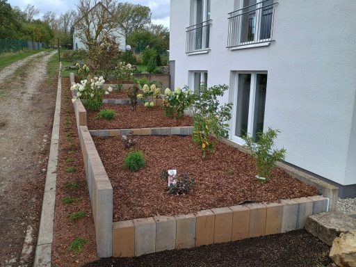 Gartenbeete mit verschiedenen Pflanzen und Kiesmulch neben einem modernen Wohnhaus.