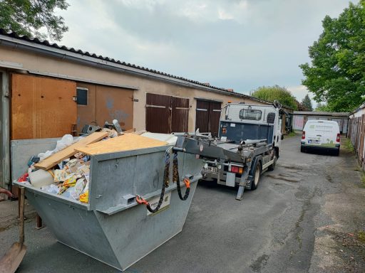 Abgestellter Container mit Bauschutt und Fahrzeug in einer engen Gasse.