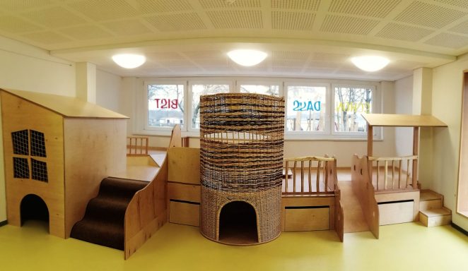 Spielzimmer mit Holzspielgeräten, darunter verschiedene Strukturen und Kletterelemente.
