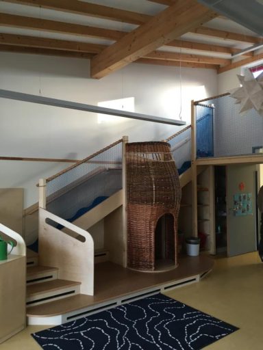 Treppenhaus mit Holzgeländer, Kletterelementen und einer Backsteinstruktur im Spielbereich.