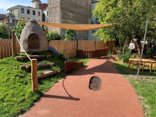 Spielplatz mit einem Spielhäuschen, Rasenflächen und einem gesäumten Weg.