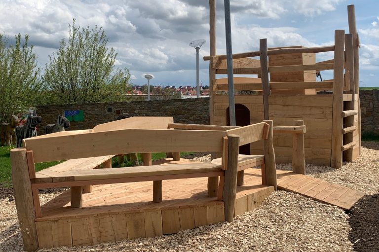 Spielplatz mit Holzspielgeräten und Sitzmöglichkeiten im Freien.