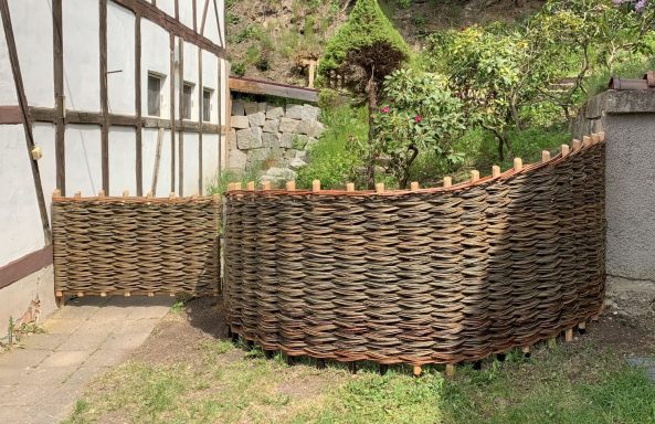 Wickelzaun um einen Garten mit einem kleinen Baum und Pflanzen.