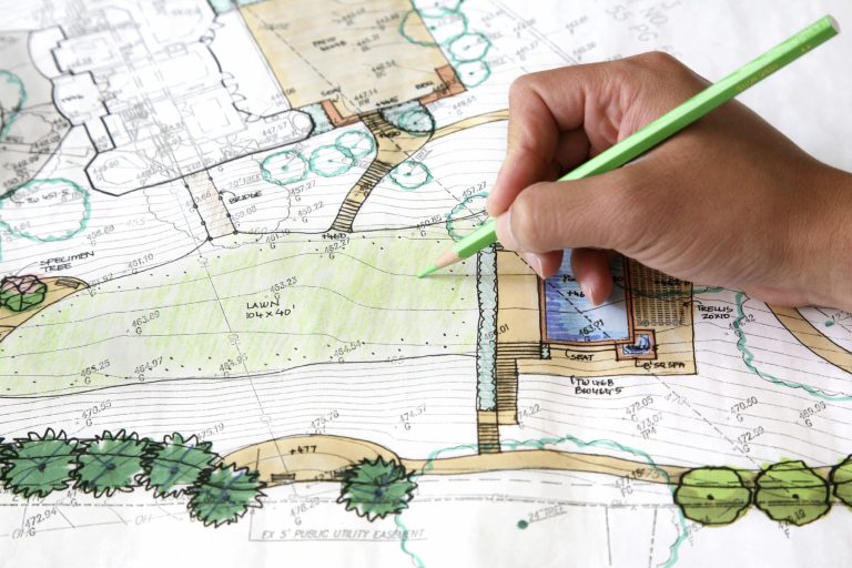 Eine Hand hält einen grünen Stift und zeichnet auf einem Gartenplan.