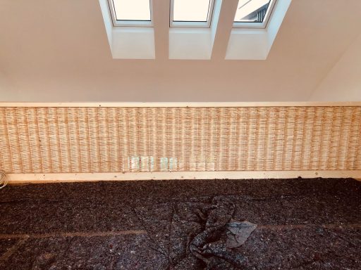 Holzvertäfelte Wand mit zwei kleinen Fenstern und dunklem Bodenbelag.