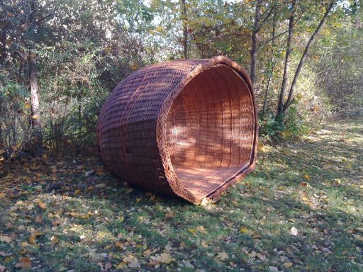 Großer, runder Korb aus Weide im Freien, umgeben von Bäumen und Gras.