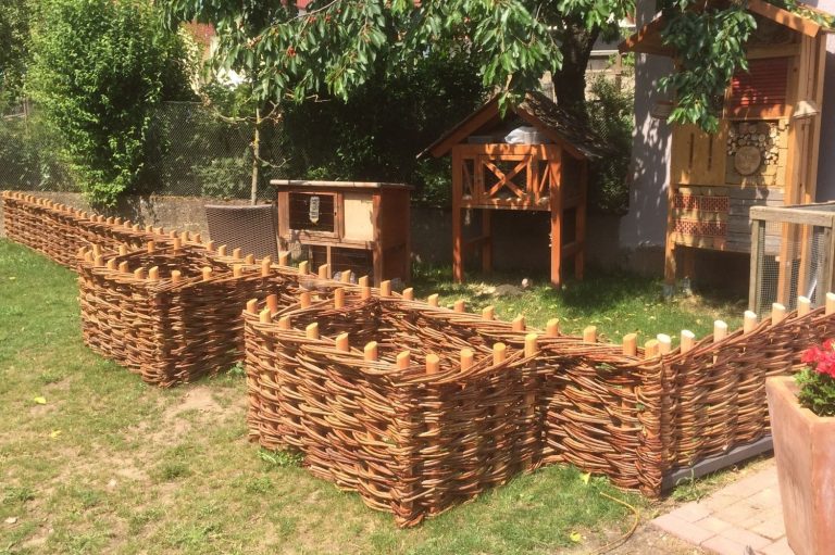 Garten mit mehreren geflochtenen Korbbeeten und einem kleinen Holzhaus im Hintergrund.