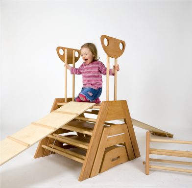 Kind spielt auf einer Holzspielgerät mit Rutsche und Kletterelementen.
