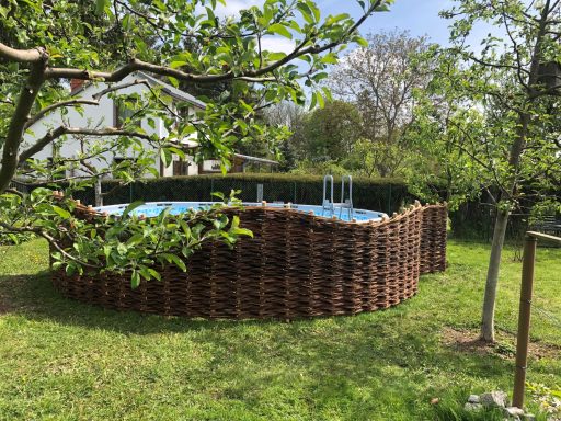 Rundes Schwimmbecken umgeben von einem geflochtenen Zaun in einem Garten.