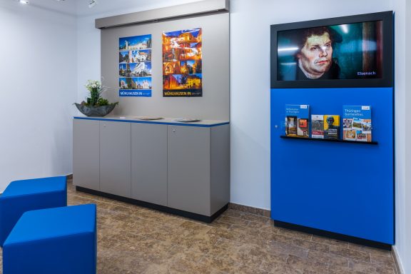 Ein moderner Raum mit blauen Sitzgelegenheiten, Bildern und einem Fernseher an der Wand.