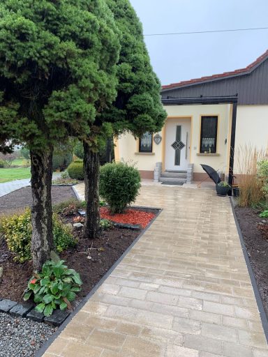 Eingang zu einem Haus mit begrüntem Weg und bepflanztem Vorgarten.