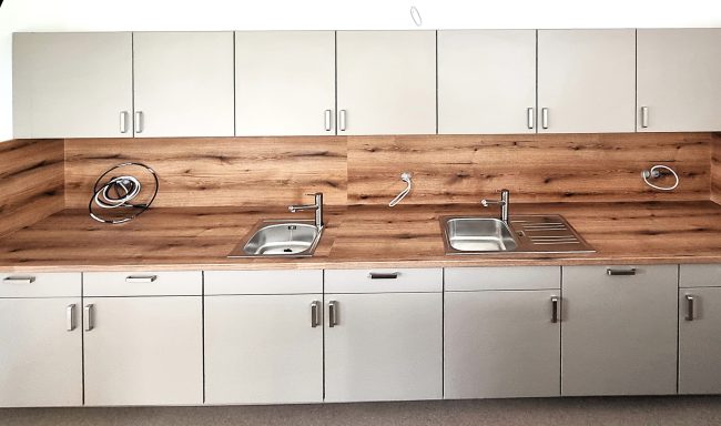 Küchenzeile mit Holzverkleidung, zwei Spülen und weißen Schränken.