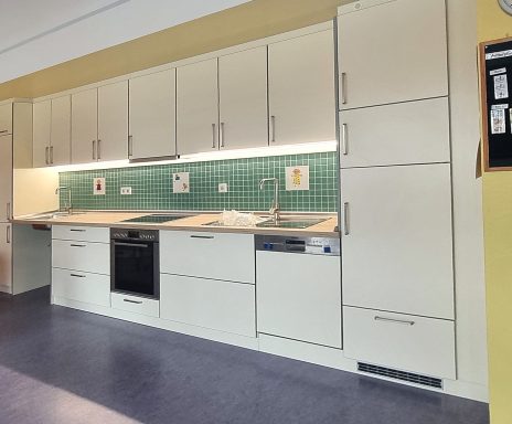 Moderne Küche mit weißen Schränken, grünen Fliesen und modernen Geräten.